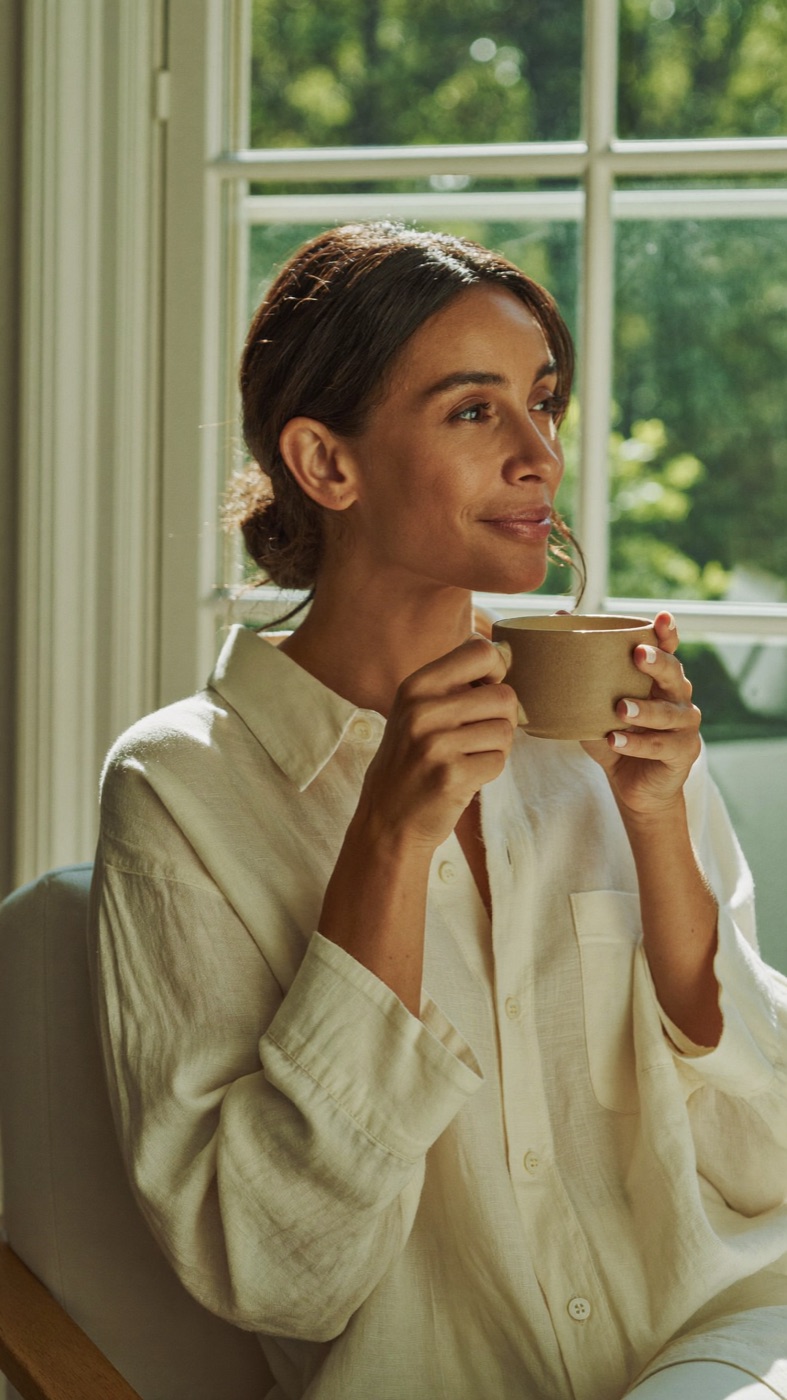 A woman relaxing with a cup of tea by a sunlit window