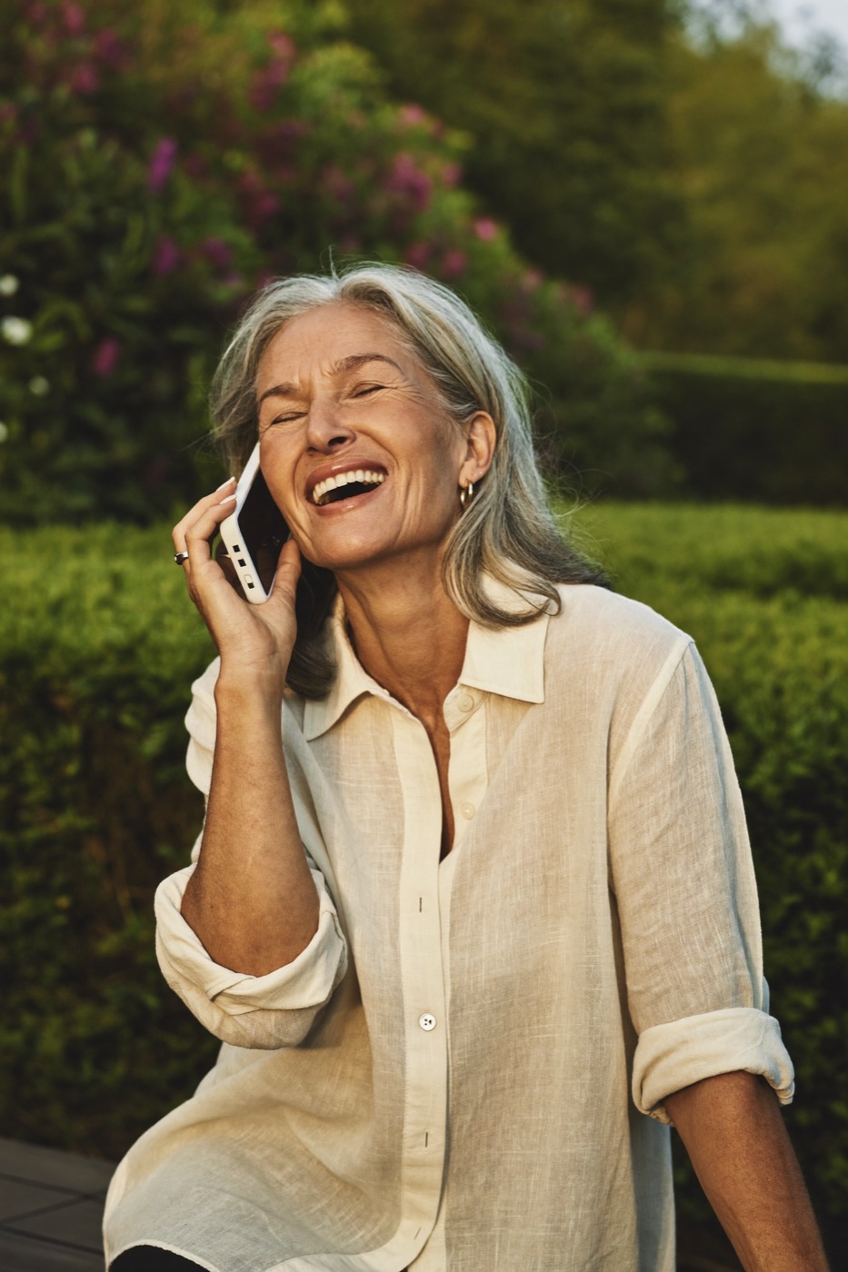 An older woman laughing on the phone in a garden