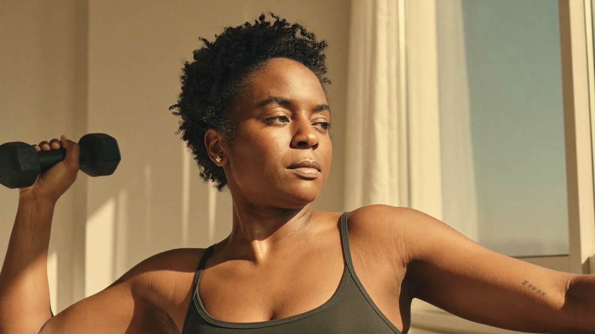 A woman lifting a dumbbell by a bright window